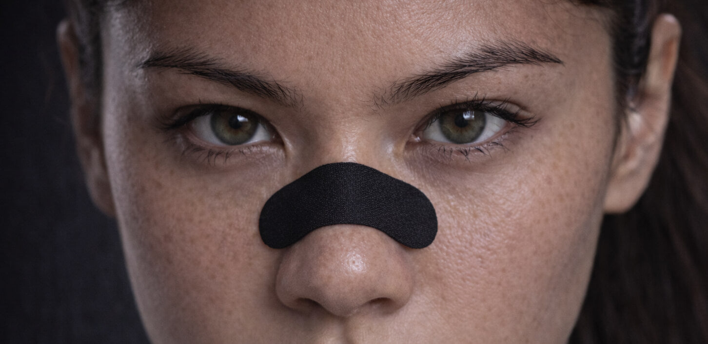 A female athletics sprinter staring intently at the camera while wearing a black BREATHMODE performance nasal strip