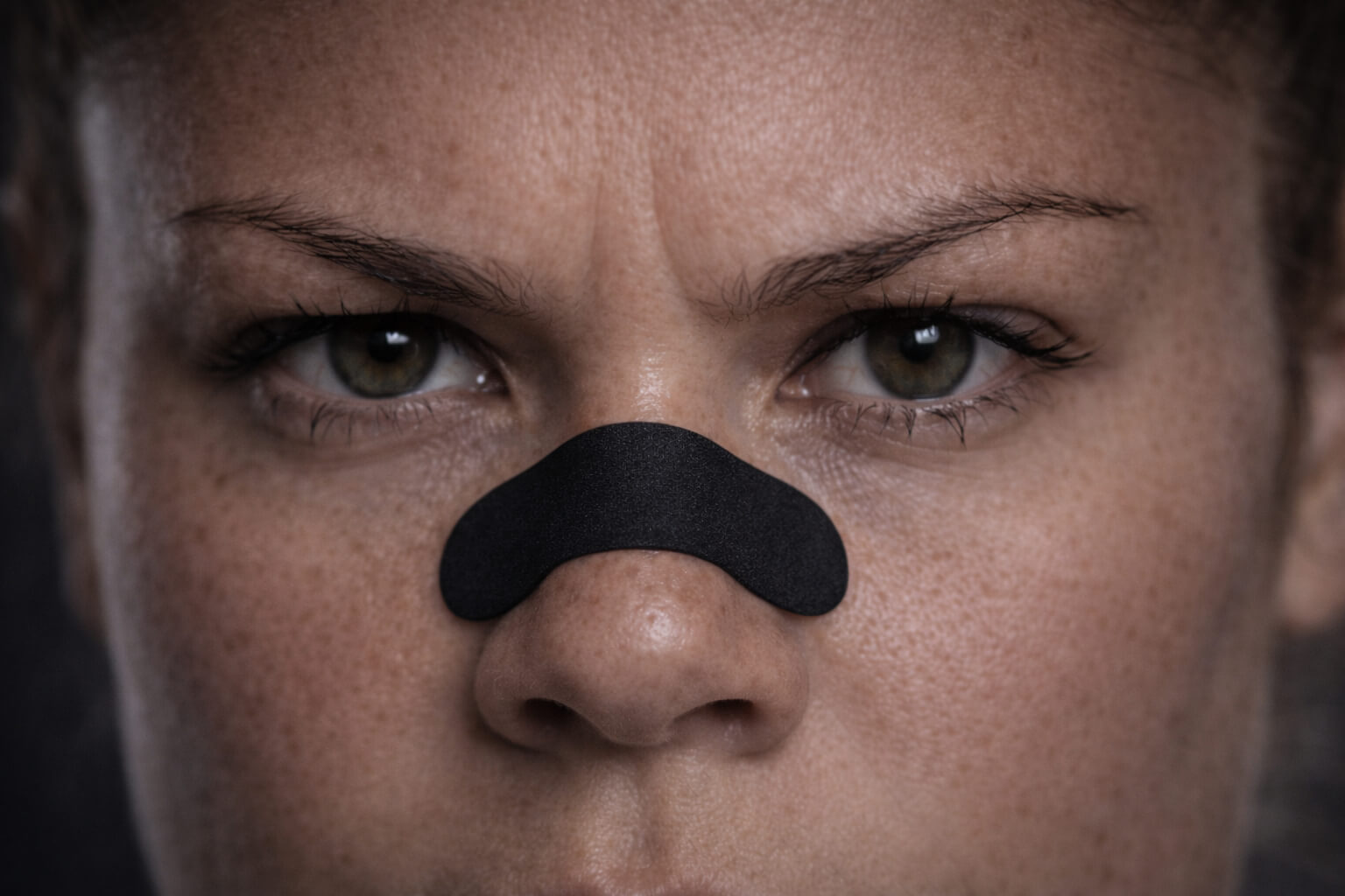 Close up of a female powerlifter athlete staring intently at the camera while wearing a black BREATHMODE performance nasal strip