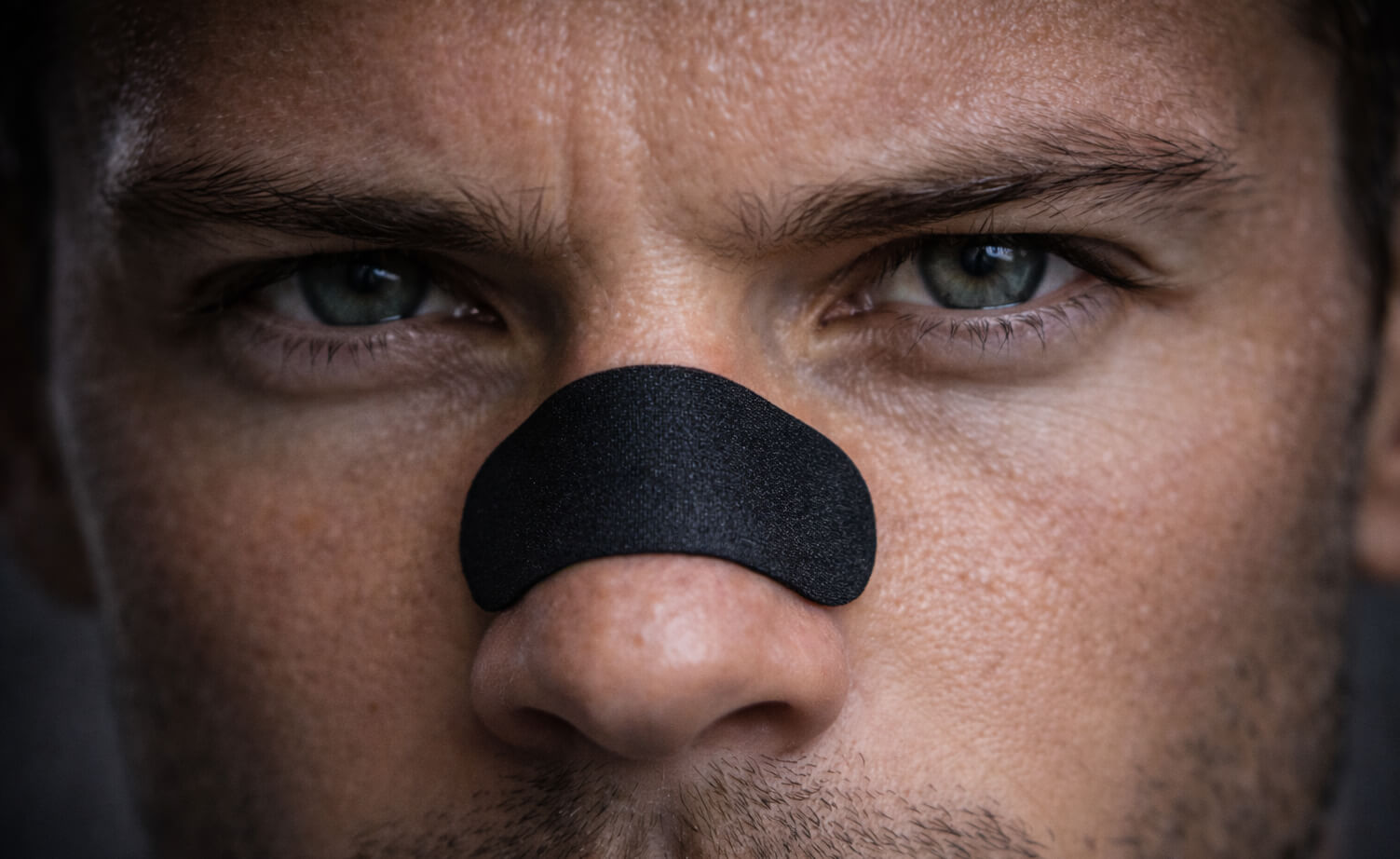 A male endurance athlete staring intently at the camera wearing a black BREATHMODE performance nasal strip