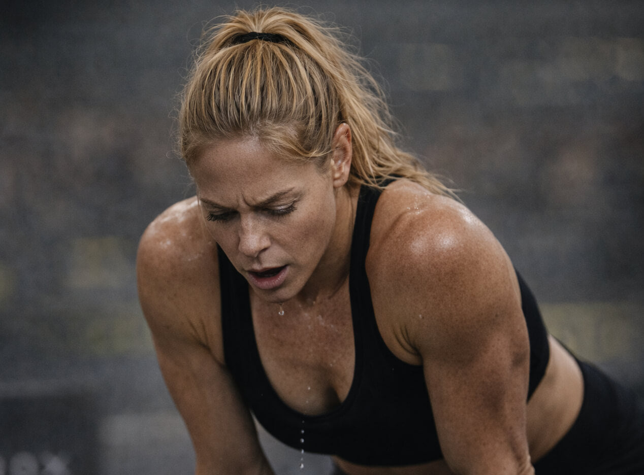 Woman in athletic wear looking exhausted & mouth breathing during a hyrox event.