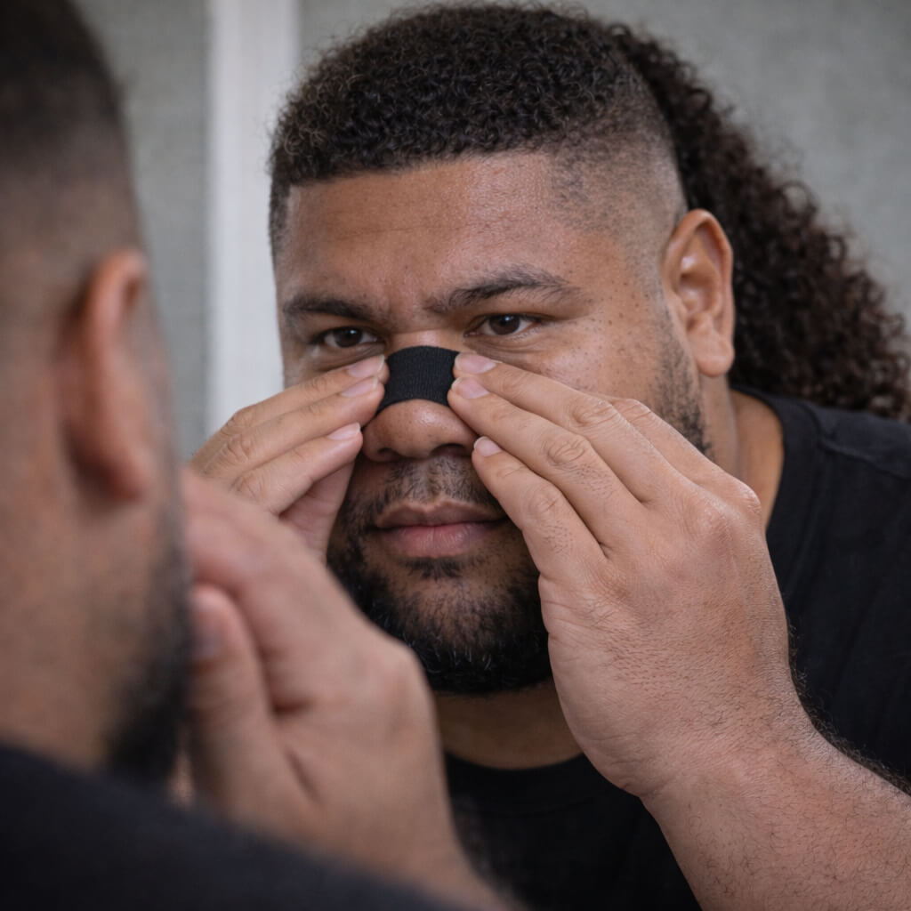 A male rugby athlete applies and presses down on a black BREATHMODE nasal strip so it sticks on properly and lasts a long time