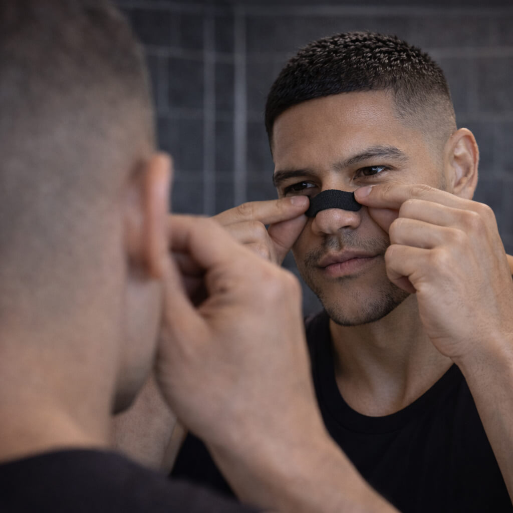 A male athlete applies a black BREATHMODE nasal strip to the perfect spot of the nose, just above the alar crease