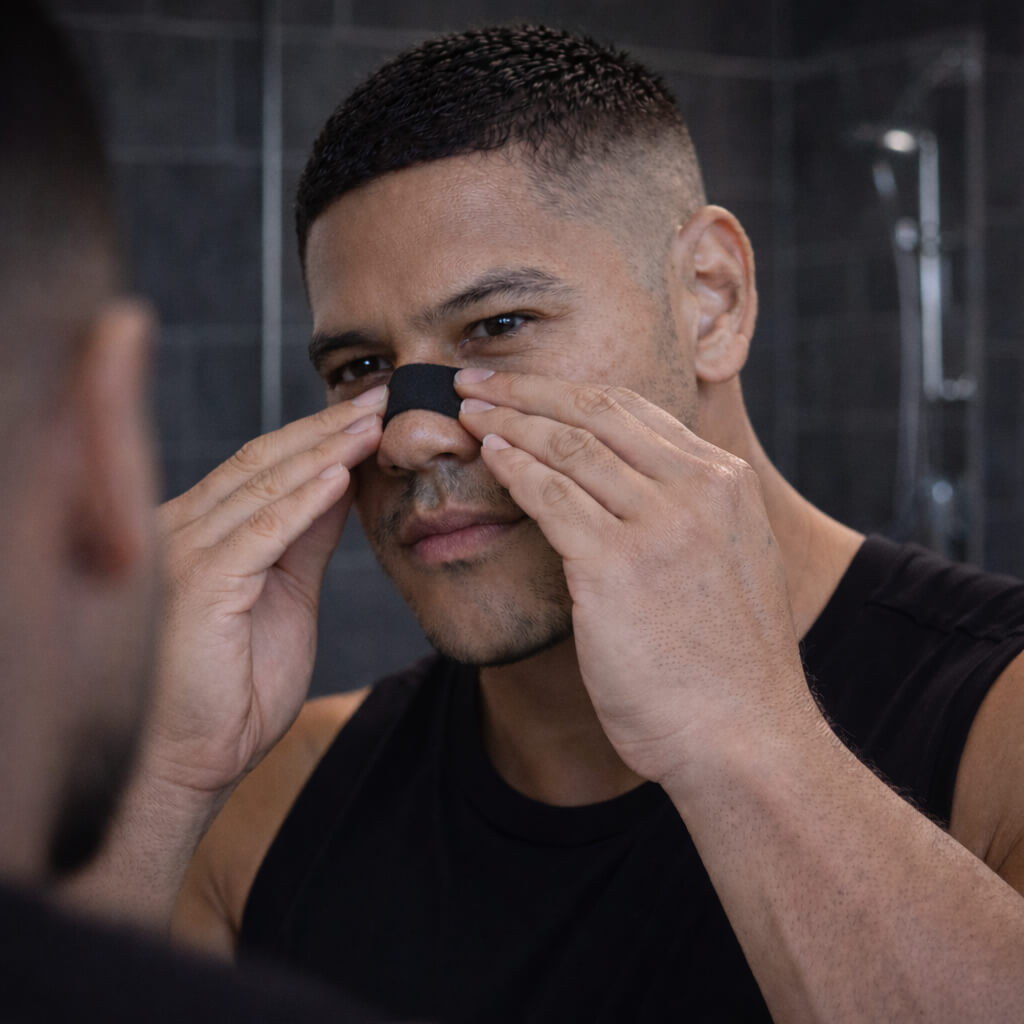 A male athlete is applying and pressing down on a BREATHMODE nasal strip to activate the adhesive for a strong 12 hour hold