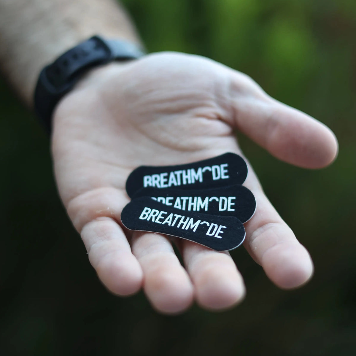 Hand holding three black BREATHMODE branded sleep nasal strips to show the free sample inside the performance nasal strips tin
