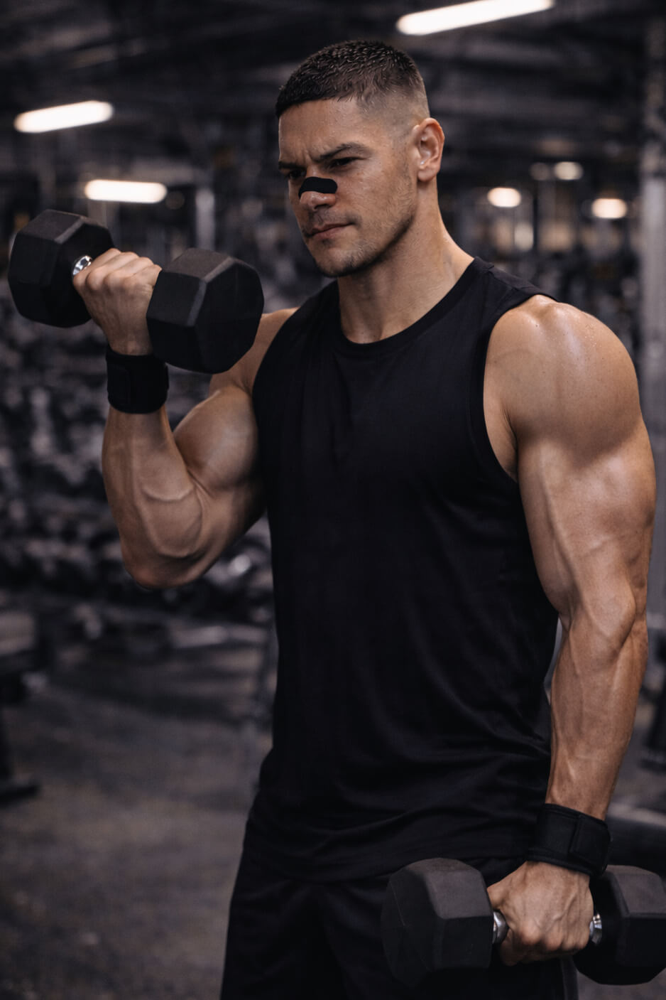 Male athlete performing bicep curls in the gym while wearing a black BREATHMODE performance nasal strip