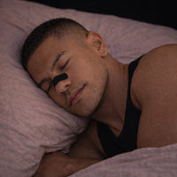 An athlete sleeping peacefully and deeply while wearing a black BREATHMODE sleep nasal strip