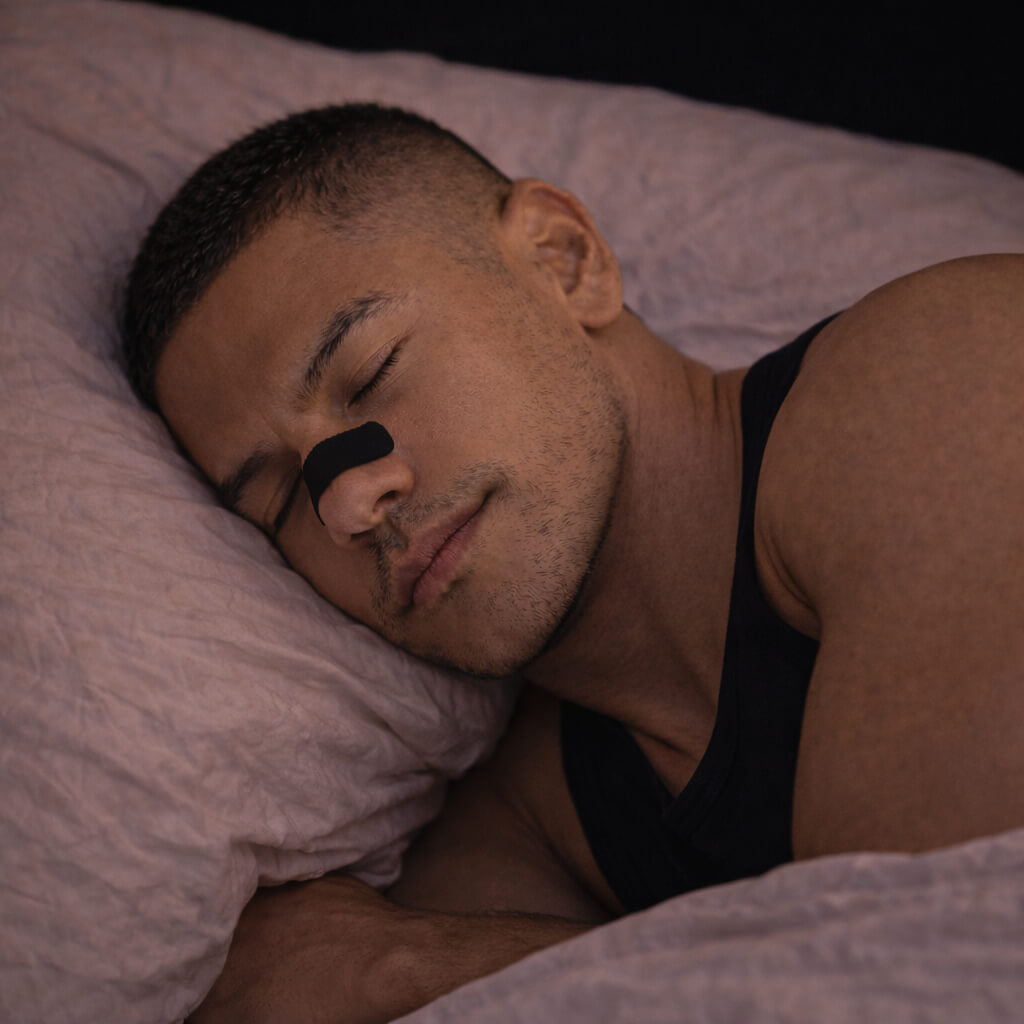 An athlete sleeping peacefully and deeply while wearing a black BREATHMODE sleep nasal strip