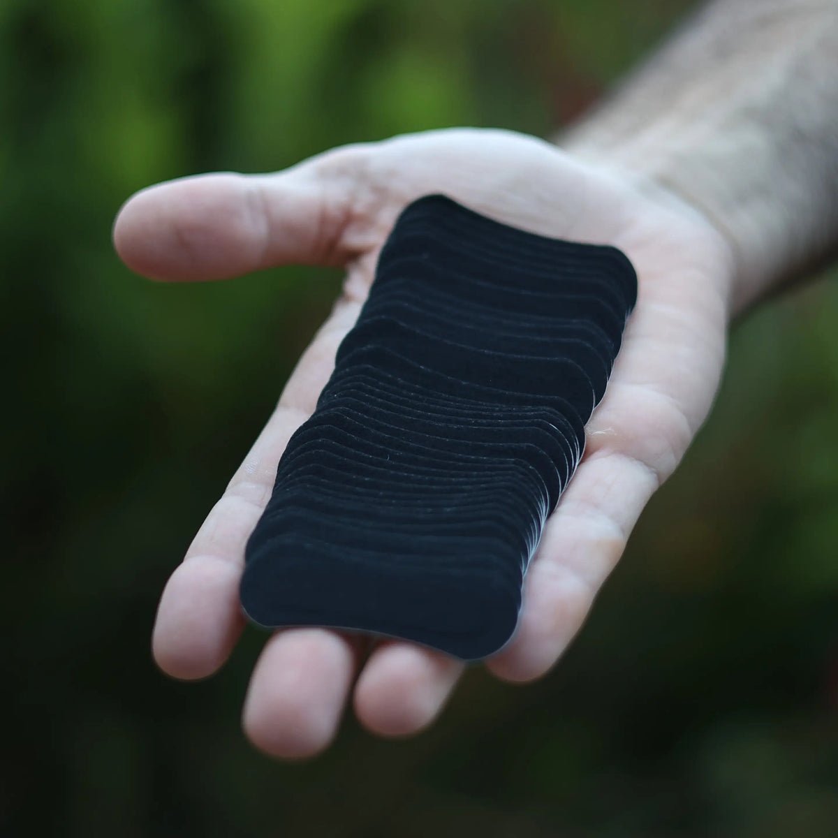 A hand holding thirty black performance nasal strips to showcase what you get in a BREATHMODE tin