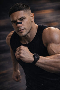 Muscular athlete in a black tank top running fast while wearing a BREATHMODE performance nasal strip