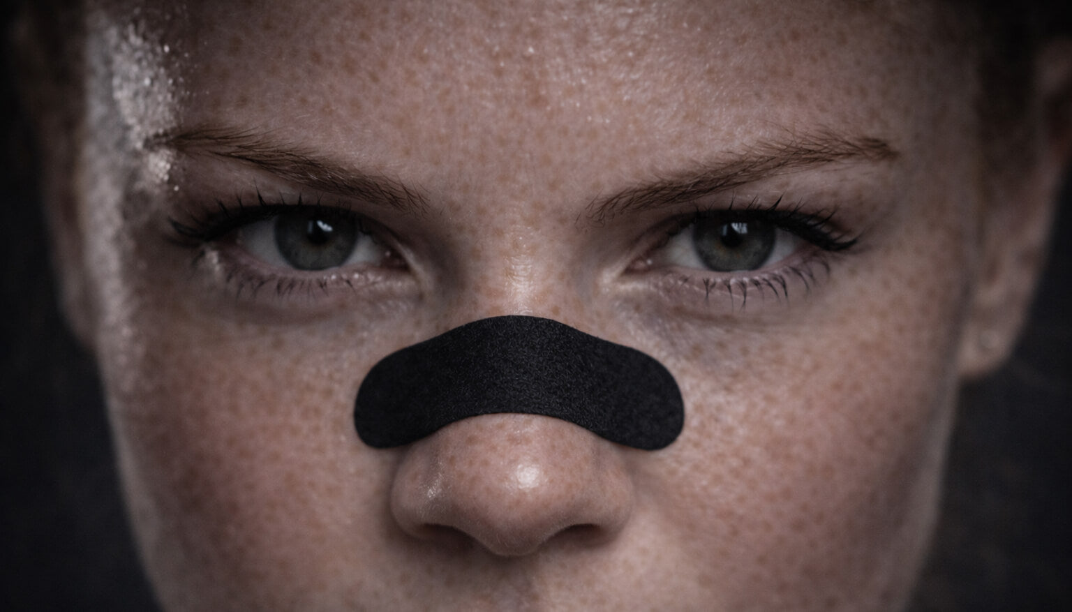 A female tennis athlete stares intently at the camera while wearing a black BREATHMODE performance nasal strip