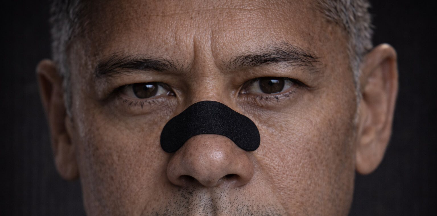 An older male athlete is staring intently at the camera wearing a black BREATHMODE performance nasal strip